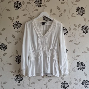 Lindex blus, Strl: 38, vit, sommar, viskos - Lindex viskosblus i storlek medium. V ringad med smock i midjan och ärmslut. Lappen med material är tyvärr bortklippt. En luftig, feminin blus med elastisk smock som accentuerar midjan på ett vacker sätt. Lång ärm med resår vid ärmslut.