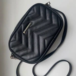 Crossbodyväska - Svart crossbodyväska från glitter. I bra skick men det finns tecken på användning, och kedjorna på bandet har tappat lite färg (se bild 4). Den stängs med dragkedja och har ett litet dragkedjefack inuti (se bild 3). Höjd: 14cm Bredd: 21cm Djup: 5cm