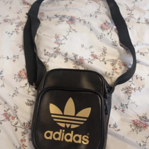 Adidas väska - Säljer en adidas väska. Det finns en liten skada på väskan som ni kan se på tredje bilden. Syns inte jätte mycket när man har på sig den. Annars är den i jätte bra skick! Säljer den billigare då skadan finns. Säljer den för 60kr + frakt!