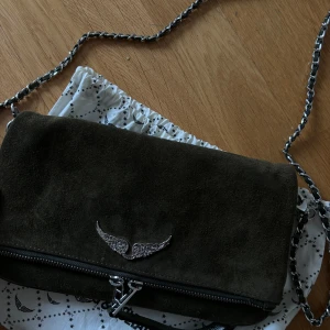 Säljer nu min älskade Zadig & Voltaire väska i grön mocka.💚💚 - Köpt för 3200 kr, i bra skick. Den saknar en frans på dragkedjan, men den kan man antingen sy på igen eller ta bort den andra om man vill det. Lite slitningar på metallen vid dragkedjan.❤️❤️ Kvitto och dustbag följer också med.