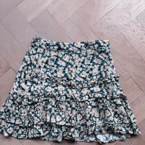 Kjol - Jag säljer en jättegullig kjol med blommor på sig. På sidan finns det en dragkedja och kjolen har volanger 💕💕