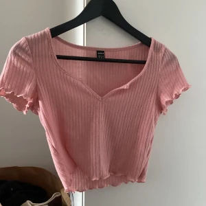 Rosa t-shirt - Säljer denna rosa t-shirt med v-ring i något stickat material. Den är lite noppig också men nästan aldrig använd.