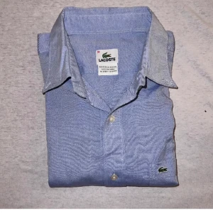 Lacoste Skjorta - Blå Lacoste Skjorta i Storlek 38. Skjortan är i använt skick så kan förekomma någon skavank men i allmänhet en fin och stilig skjorta. Skriv vid minsta fundering eller om fler bilder önskas. Prisförslag välkomnas👍 FLER LIKNANDE PLAGG PÅ PROFILEN 65
