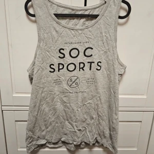 Grå linnetopp från SOC - En grå linnetopp från SOC med tryck på framsidan. Toppen har en rund halsringning och är ärmlös, vilket gör den perfekt för träning eller varma sommardagar.