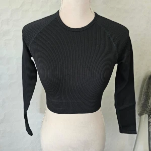 Svart ribbad croppad topp från amn - En svart ribbad croppad topp från aim'n med långa ärmar. Toppen har en tight passform och är tillverkad av en blandning av polyamid och elastan.