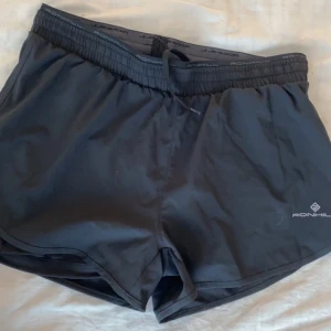 Svarta träningsshorts från Ronhill - Ett par svarta träningsshorts från Ronhill. Shortsen har en elastisk midja med dragsko och är tillverkade i ett lätt och bekvämt material.