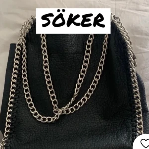 Svart handväska med kedjedetaljer - jag SÖKER En elegant svart handväska med kedjedetaljer. Väskan har en stilren design och är tillverkad av ett material som liknar skinn. SÖKER TIAMO