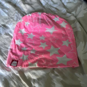 Rosa mössa med vita stjärnor - En rosa mössa med vita stjärnor. Mössan har en enkel design med ett litet märke på sidan.