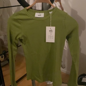 Grön ribbad tröja från JJXX - En grön ribbad tröja från JJXX med långa ärmar. Tröjan har en rund halsringning och är i storlek M.