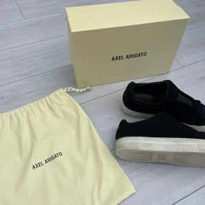 arigato sneakers - Svarta arigato skor i mocka material, utan snören. Väl använda men i bra skick för att vara använda. Impregnerade kontinuerligt. Låda+påse finns kvar och fås med vid köp. 