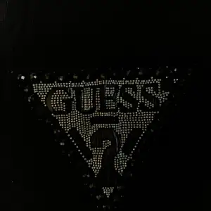 Ett svart linne från Guess med glittriga stenar och Guess-logotypen. Tillverkat av 100% ekologisk bomull. Jag har köpt den här på Plick, men då jag inte använder säljer jag vidare. Nyskick. Storlek L, men passar även M och XL etc.