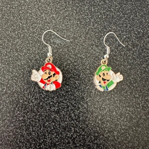 Örhängen med Mario och Luigi motiv - Ett par örhängen med motiv av Mario och Luigi från ett populärt spel. Mario är klädd i rött och Luigi i grönt. Örhängena har krokfästen i silverfärg. krokarna är inköpta som nickelsäkra.