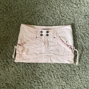 Lågmidjad kjol - Så himla cool ljusrosa, lågmidjad jeanskjol med snygga detaljer!! Midjemått: ca 42 cm, längd fram: ca 27 cm, längd bak: ca 31 cm