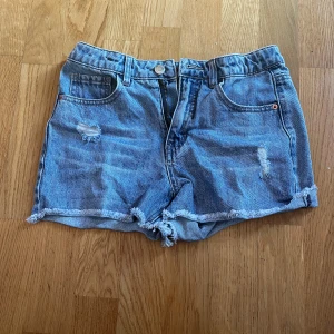 Blå jeansshorts från LAB - Ett par blå jeansshorts från LAB med slitna detaljer och upprullade kanter. Shortsen har fem fickor och en knapp- och dragkedjestängning framtill.