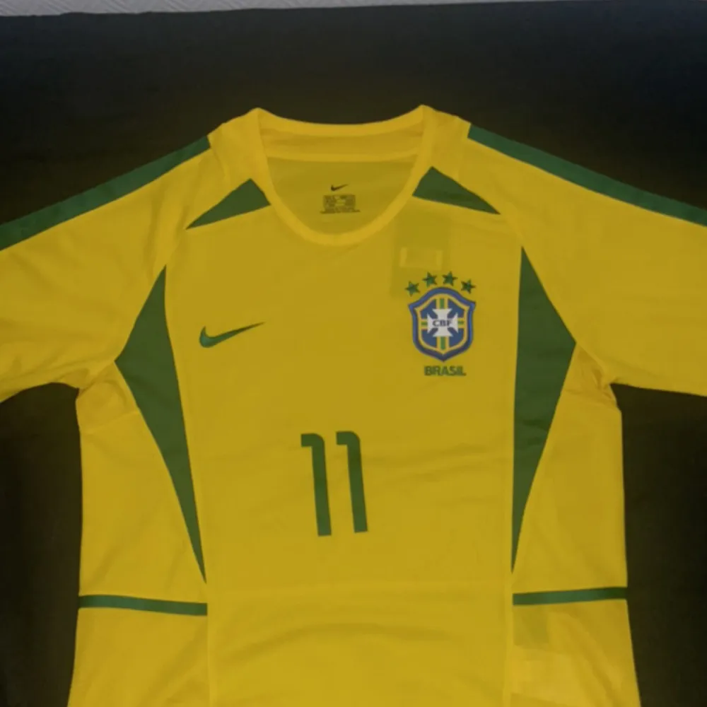 Fet retro Brasilien fotbollströja med ikonen Ronaldinho 11 på ryggen🇧🇷. Säljer pågrund av liten storlek. Perfekt till sommaren. Tröjan är helt ny med etikett kvar. Fick den i present. Skriv vid funderingar.. Sport & träning.