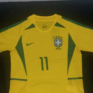 Fet retro Brasilien fotbollströja med ikonen Ronaldinho 11 på ryggen🇧🇷. Säljer pågrund av liten storlek. Perfekt till sommaren. Tröjan är helt ny med etikett kvar. Fick den i present. Skriv vid funderingar.
