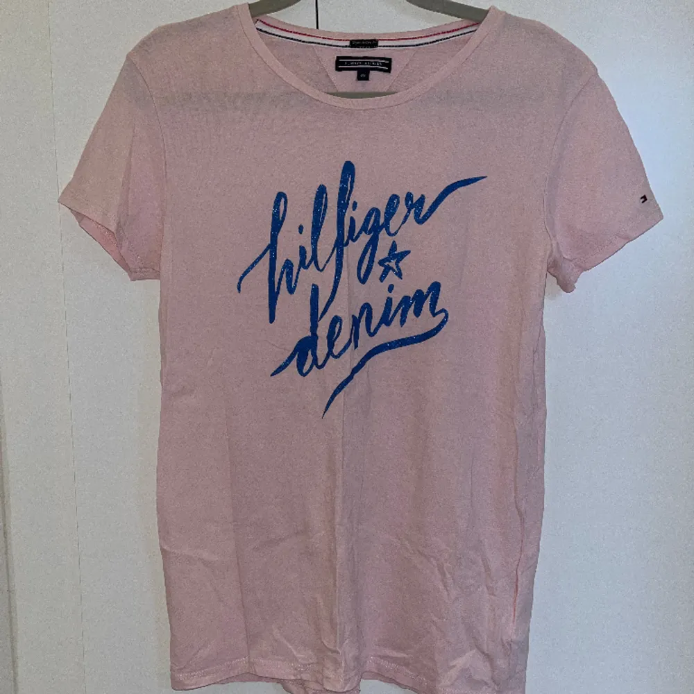 Tommy Hilfiger t-shirt i ljusrosa med ett blått tryck fram. Endast använd några enstaka gånger. Storlek 176 men passar en Xs.🩷. T-shirts.