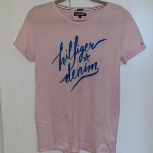 Tommy Hilfiger t-shirt i ljusrosa med ett blått tryck fram. Endast använd några enstaka gånger. Storlek 176 men passar en Xs.🩷
