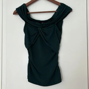 Festtopp - Så fin draperad topp. Går att ha off shoulder. Perfekt till fest eller vardags. Superbra skick!! Obs den är mörkgrön inte svart!