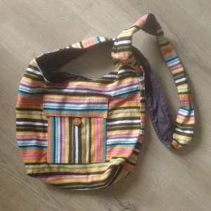 Väska - Vintage tygväska i jättebra skick. Slitstarkt vävt yttertyg. 3 fickor: en ytter och en inner + liten ficka i axelremmen. Väskans öppning stängs med dragkedja. Mått : 26 cm lång 36 cm bred 10 cm djup (mätt i botten) 