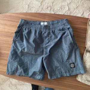 Stone island  - Shorts i grått med Stone Island-logotypen på vänster ben. Shortsen har en elastisk midja och två fickor på sidorna. Reflex