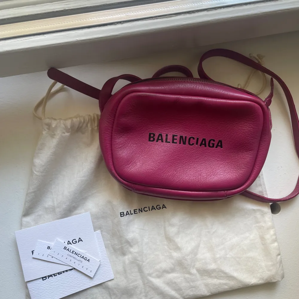 Säljer min coola Balenciaga väska i modellen camera bag i en rosa jätte fin färg! Väskan är flitigt använd därmed har den släppt lite i bandet (se bilder), men går att laga med textil limm. Till utseendet har den inga  defekter i färg osv.  . Väskor.