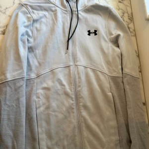 Ljusgrå under armour luvtröja  - En relativt ny ljusgrå under armour hoodie. Storleken är S och passformen är relativt tajt på kroppen. Hoodien är perfekt för kallare sommar dagar eller sen vår/tidig höst. Tröjan är aningen tunn och sitter perfekt runt magen men med mer utrymme.