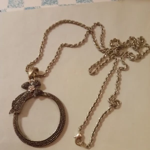 Halsband med hänge av ett förstoringsglas mönstrad Silverfärgad . - Vackert halsband med hänge av ett förstoringsglas mönstrad Silverfärgad och vit sten .