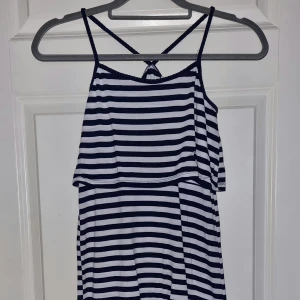 Randig sommarklänning - En randig sommarklänning med smala axelband och korsad rygg. Klänningen har ett löst sittande överdel och är i en lång modell. Färgerna är marinblå och vit. Från H&M i stl 146/152