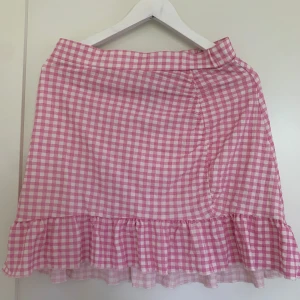 Rutig kjol - Jag säljer en rosa rutig kjol i storlek L som har använts en del men är i ett bra skick! Kjolen har en liten volang ner till och kan passa en som bär storlek M också! 
