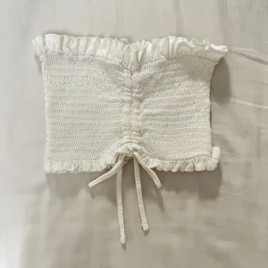 Bikbok vit tubtopp med volang och rosett - Säljer denna tubtopp med volang- och rosettdetalj då storleken inte passar. Nyskick då den används 1/2 gånger. Har utgått ur sortimentet. 