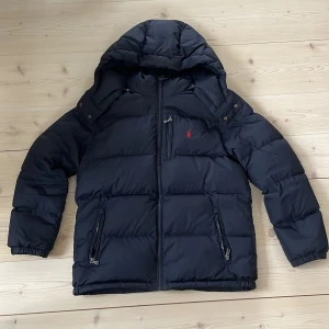 Polo Ralph Lauren vinterjacka - Polo Ralph Lauren vinterjacka som passar perfekt på mig som är 165cm lång. Jackan är för 14-16 år och är mörkblå med rött märke. Jackan är i nyskick och använd ett fåtal gånger.