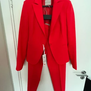 Rinascimento kostym  - Figursydd kavaj med tillhörande cigarettbyxor corallröda köpt på Monti för 3 år sedan . Aldrig använda. Nypris 2500kr