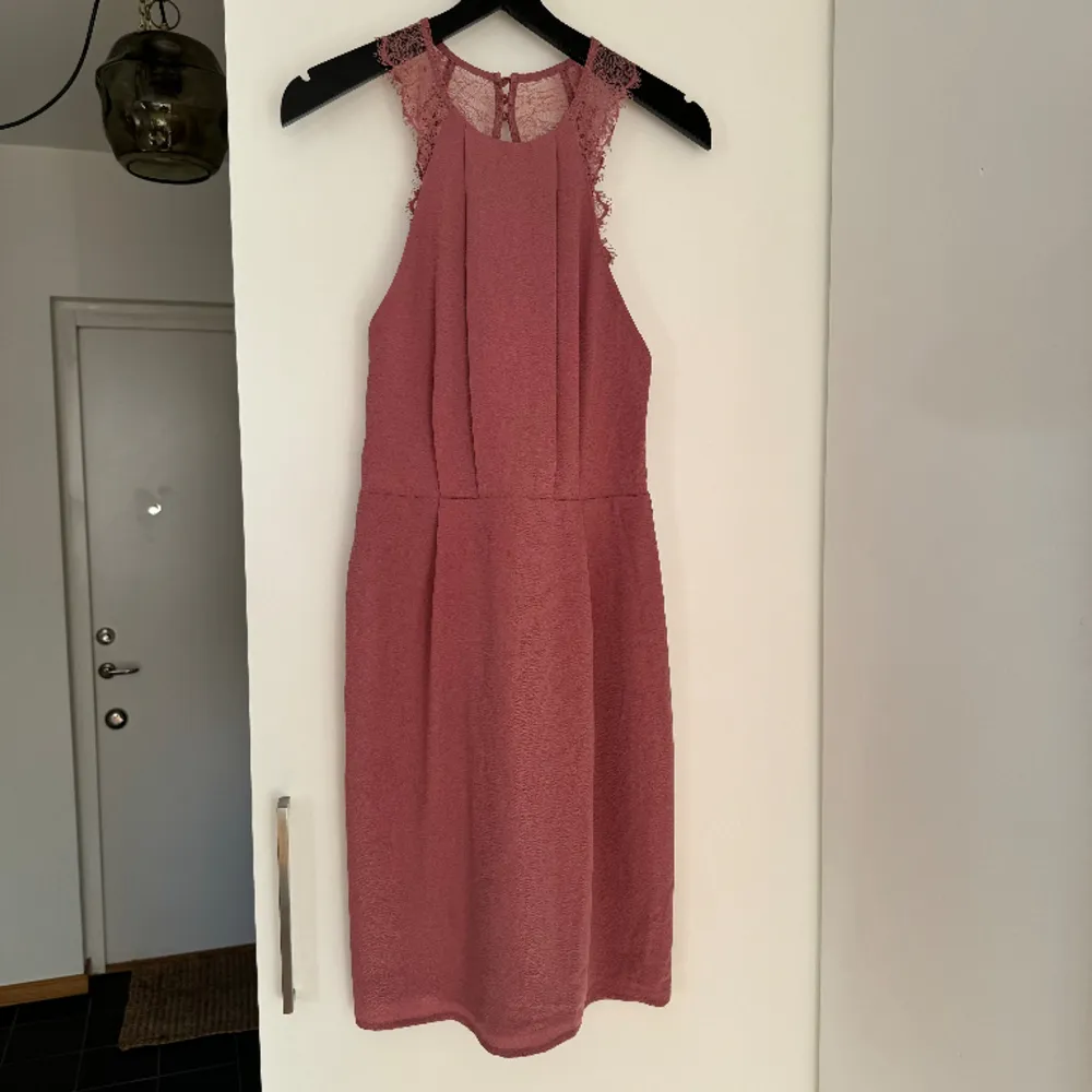 Ärmlös klänning med spetsdetaljer i dusty pink-nyans. Öppen rygg med knappar i nacken och dragkedja i svanken. Insydd underklänning. Något nopprig på ena sidan (se bild 3). Använd en gång.. Klänningar.