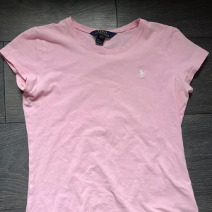 Polo Ralph Lauren t-shirt - Rosa Polo Ralph Lauren t-shirt som är i bra skick men tyvärr för liten. På lappen står det L men de är i ”barnstorlekar” den sitter som xs ❤️ Pris kan diskuteras!!