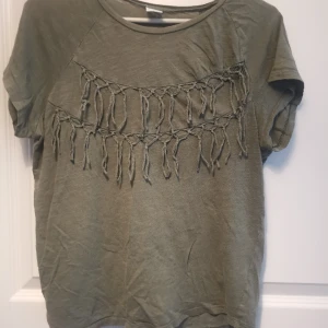 Grön topp med fransar - Häftig t-shirt/ topp i mossgrönt med knutar och fransar framtill, lite asymmetrisk, kortärmad