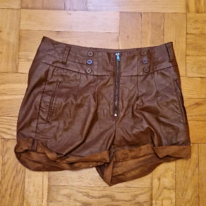 Bruna shorts i fejkläder - Bruna shorts i fejkläder med dragkedja och knappar för syns skull. Från Kappahl. Okej att komma med egna bud. Katt i hemmet. 
