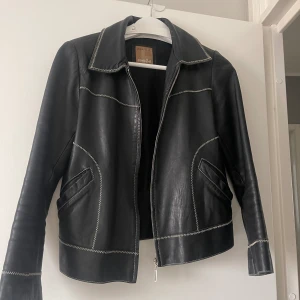 Tunn Skinnjacka - Säljer denna tunna skinnjacka med vita sömmar. Dragkedjan fungerar ej och den var trasig när jag köpte den på humana men den går nog att fixa! Lite kortare modell. 