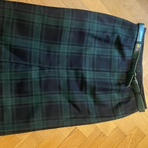 Tartanrutig kjol - snyggt skuren halvlång (70 cm) pennkjol i lättskött rayon/polyester med ullkänsla. Sprund fram och bak, fodrad. 78 cm i midjan. Skärp medföljer. Mkt fint skick, använd fåtal gånger. Dansk tillverkning