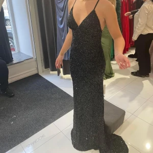 Oanvänd balklänning - En svart paljettbalklänning med öppen och vacker rygg. Storlek 36/38. Prislappen sitter kvar. Aldrig använd. Jag hittade en annan klänning som passade mig mer i färgen, därför säljer jag denna. Köpt för 4990kr, säljer för 3000kr