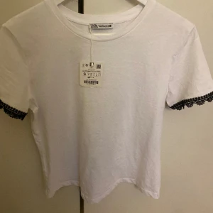 Tröja med brodering  - Säljer en t shirt med svart brodering från zara. Den är i nyskick och oanvänd då den tyvärr var en för stor storlek. Kom privat för mer bilder! 🩷