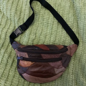 Patchwork-läderväska - Snygg, vintage midjeväska i patchwork-mönster. Justerbar rem så går att bära på olika sätt beroende på hur man vill ha den. I läder och i bra skick förutom några slitningar enligt bild, men ingenting som stör helhetsintrycket. 