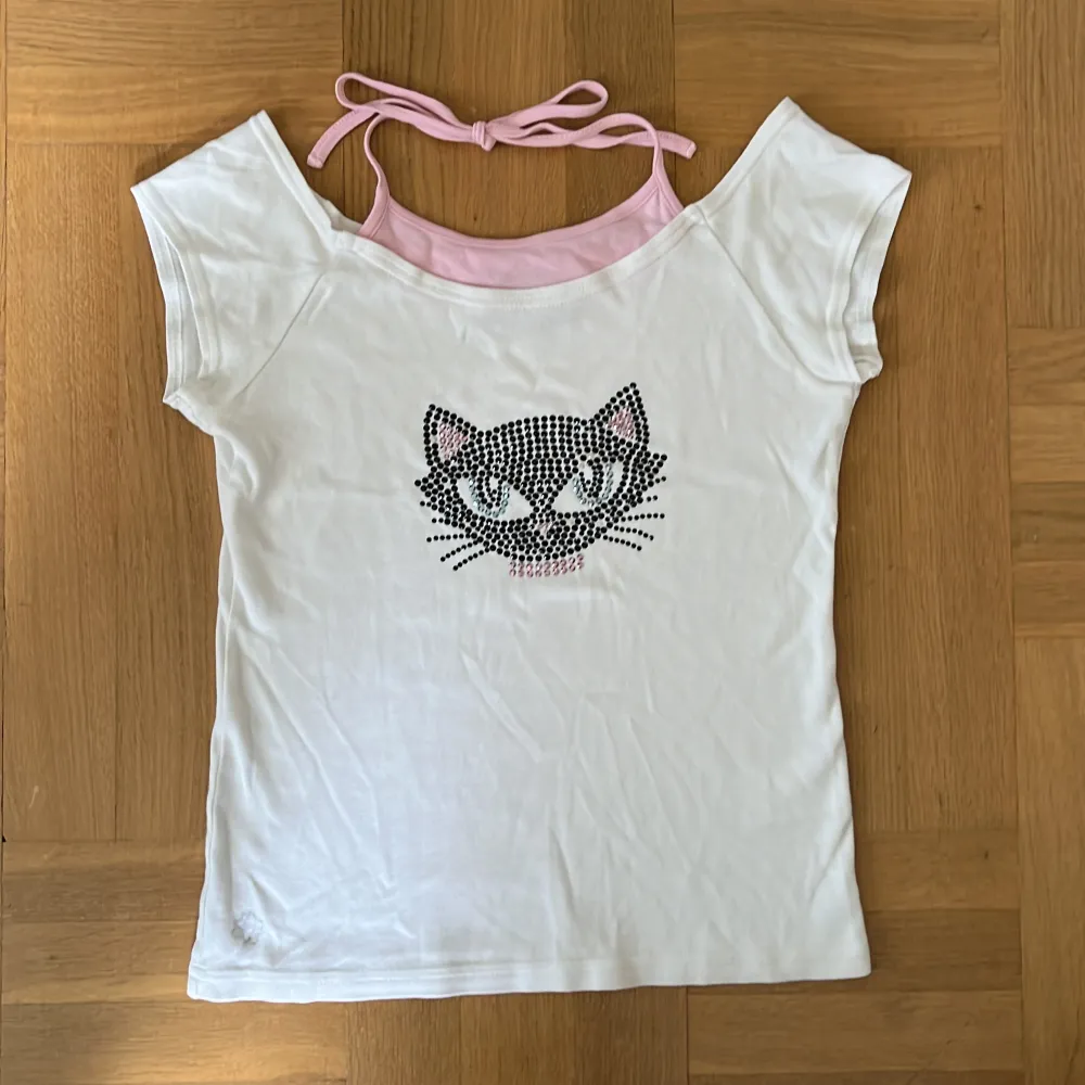 Vit barn t-shirt med katt gjort av strass. Med rosa knytband i nacken. Stolek: 158/164. T-shirts.