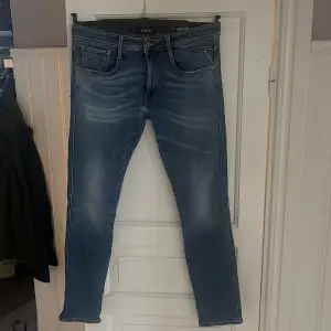 Ett par stilrena replay anbass jeans med ett litet litet hål  Strl 34/32