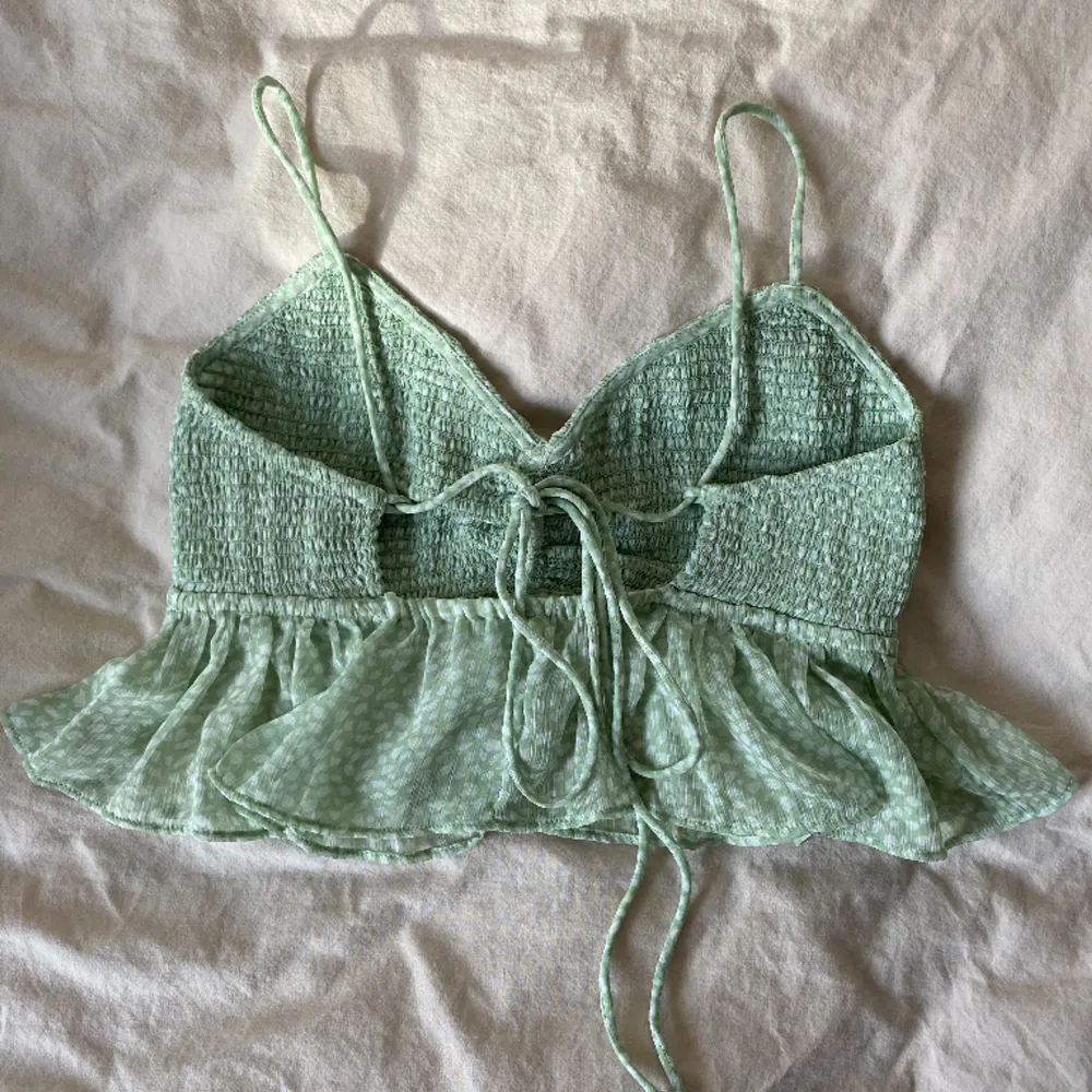 Supersöt grön topp från Gina Tricot! Ett somrigt linne med vitt mönster och knytning i ryggen. Något kortare i modellen med en volang nertill. Storleken går att justera med knytningen . Toppar.