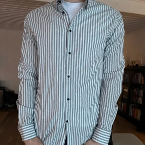 J.Lindeberg randig skjorta - Säljer min oanvända grå/vit randiga skjorta från J.Lindeberg. Helt ny utan prislapp.
