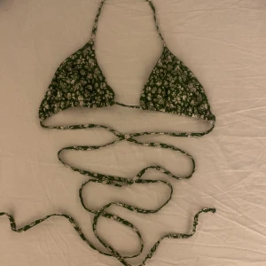 Söt bikini överdel - En supersöt bikini överdel från & other stories, grön med vita detaljer på. Knyte runt halsen samt ett längre knyte som går att knyta runt kroppen flera gånger. Storleken är 38. Bikinin köptes för några/något år sedan och är använd ett fåtal gånger. 