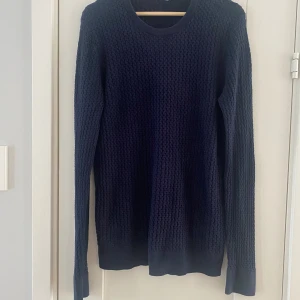 Marinblå stickad tröja från J.Lindeberg i strl M, modell Ryan Urban braid - Använd men i fint begagnat skick.  Mått Över axeln: ca 44 cm Längd från axeln och ner: ca 75 cm  100% bomull   Kommer från ett djur och rökfritt hem.
