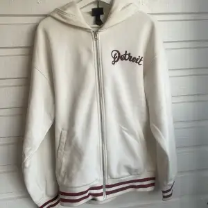 Detroit ziphoodie i vit och röd färg. Köpt på H&M för nått år sedan (sällsynt) och endast använd fåtal gånger Tröjan e lite baggy  Skick:9/10 Storlek: S 