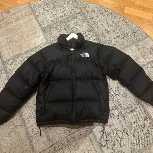 THE NORTH FACE puffer jacket  - En snygg, stilren och tidlös jacka.  The North Face Wmns 1996 Retro Nuptse Jacket Blk - Vattenavstötande - Justerbara Velcro® muddflikar - Luva som kan stoppas undan - Ripstop med DWR-hölje - Innerficka med blixtlås - High fill, Responsible Down 